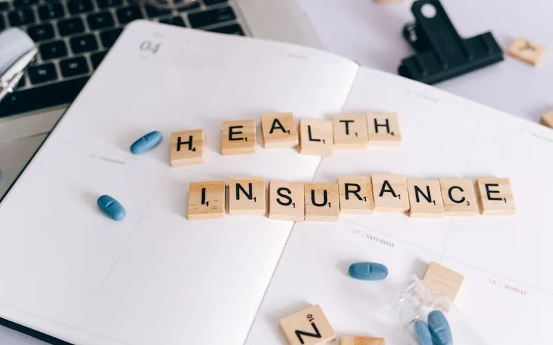 Lettres Scrabble Health Insurance sur agenda avec comprimés illustrant la mutuelle obligatoire en pharmacie